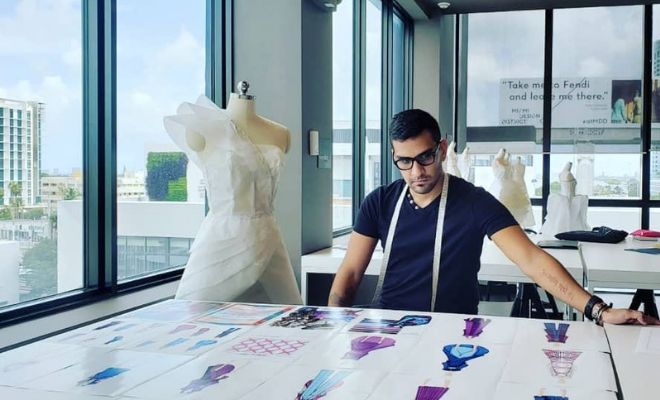 project runway winner sebastian grey sitting on a desk surrounded by fashion sketches