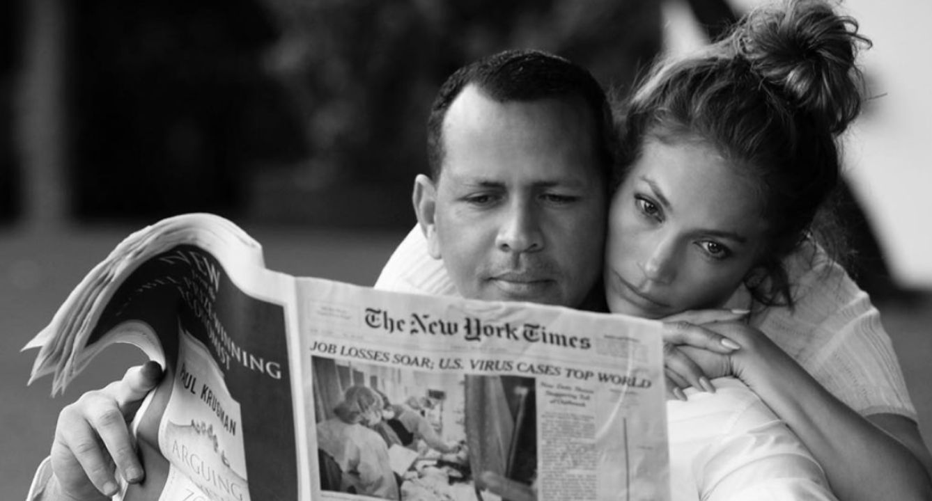Jennifer Lopez cuddling with Alex Rddriguez who is reading a newspaper