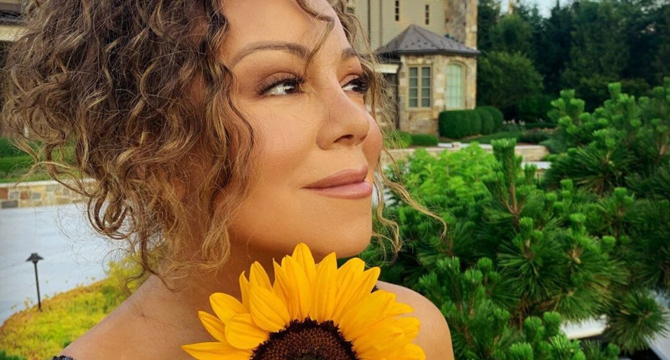 Mariah Carey photographed outdoors while holding a yellow sunflower