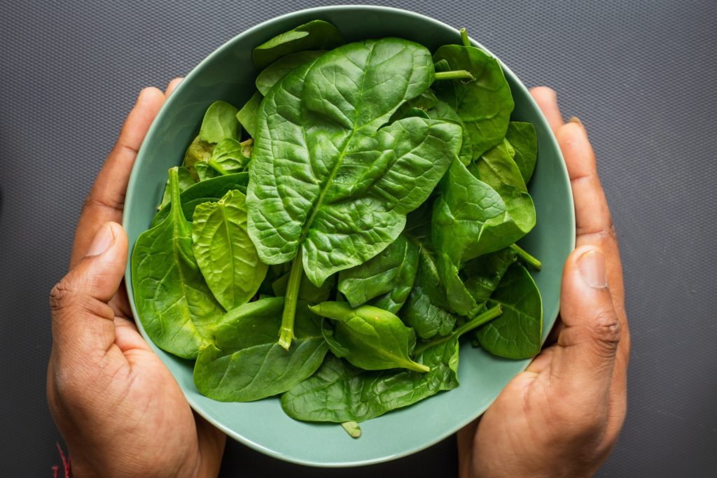 Person holding a bowl of spinach