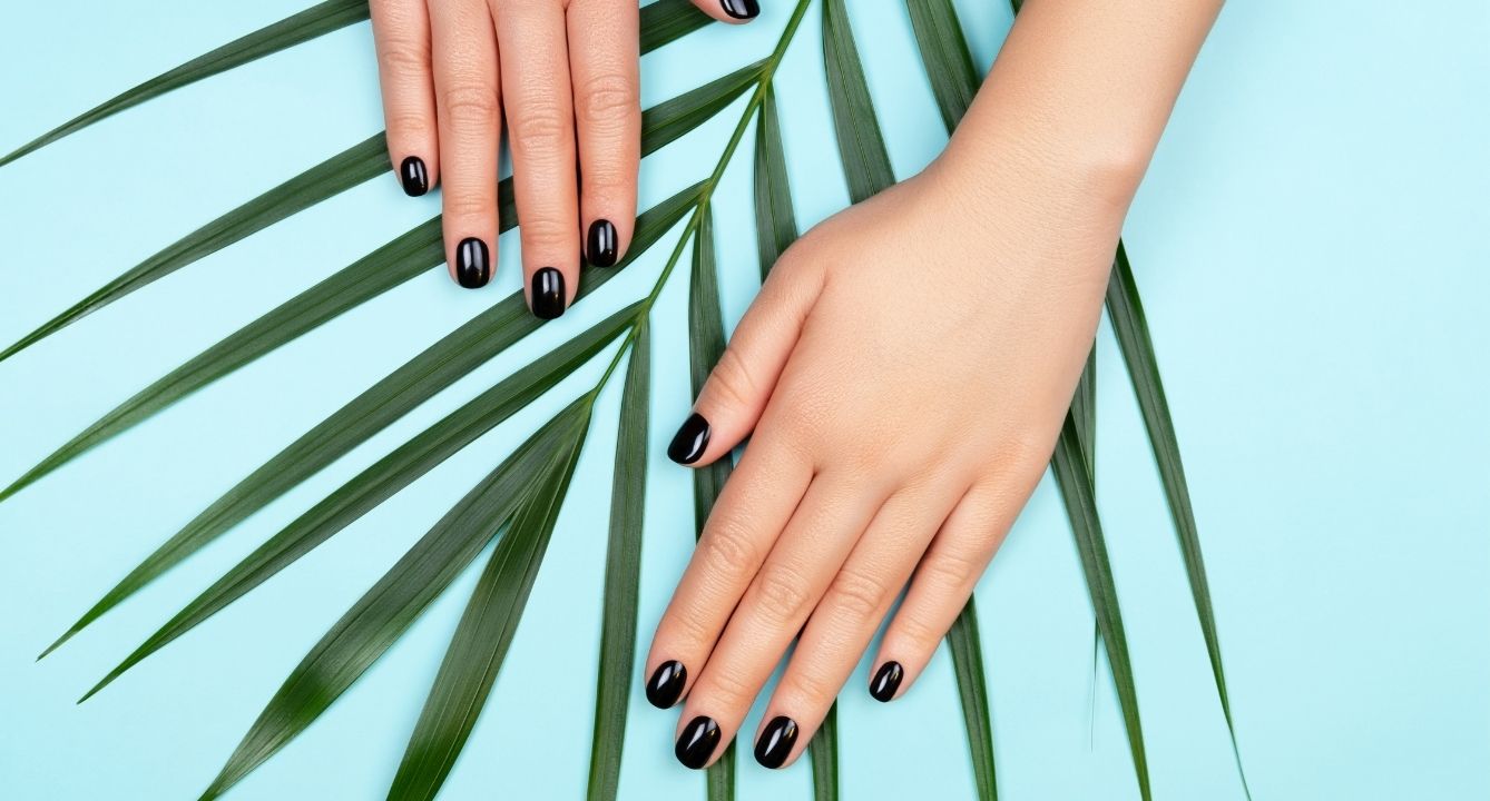 hand with black nails posing on palm leaf